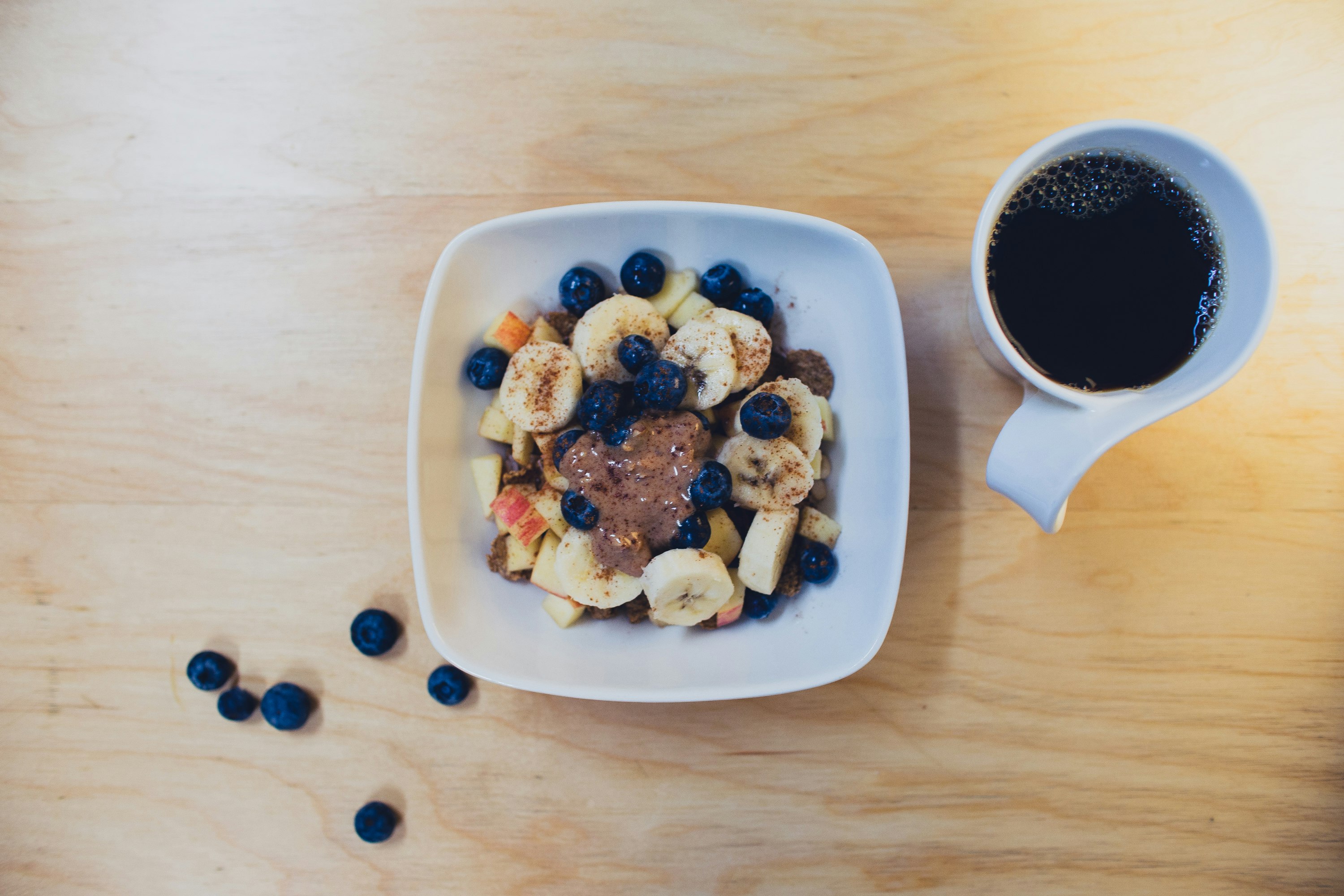 sliced bananas with berries and peanut butter beside cup of coffee on table